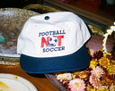 White cap with 'Football Not Soccer' text on a table with decorative elements